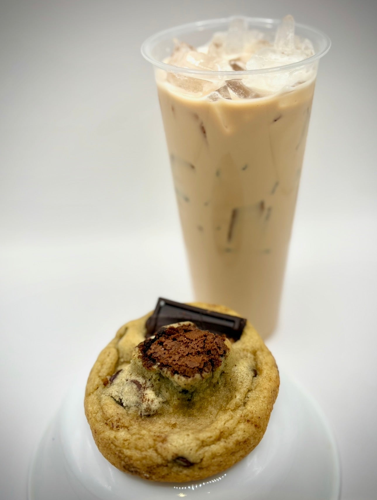 Cookie with a chocolate bar on top next to an iced coffee drink.