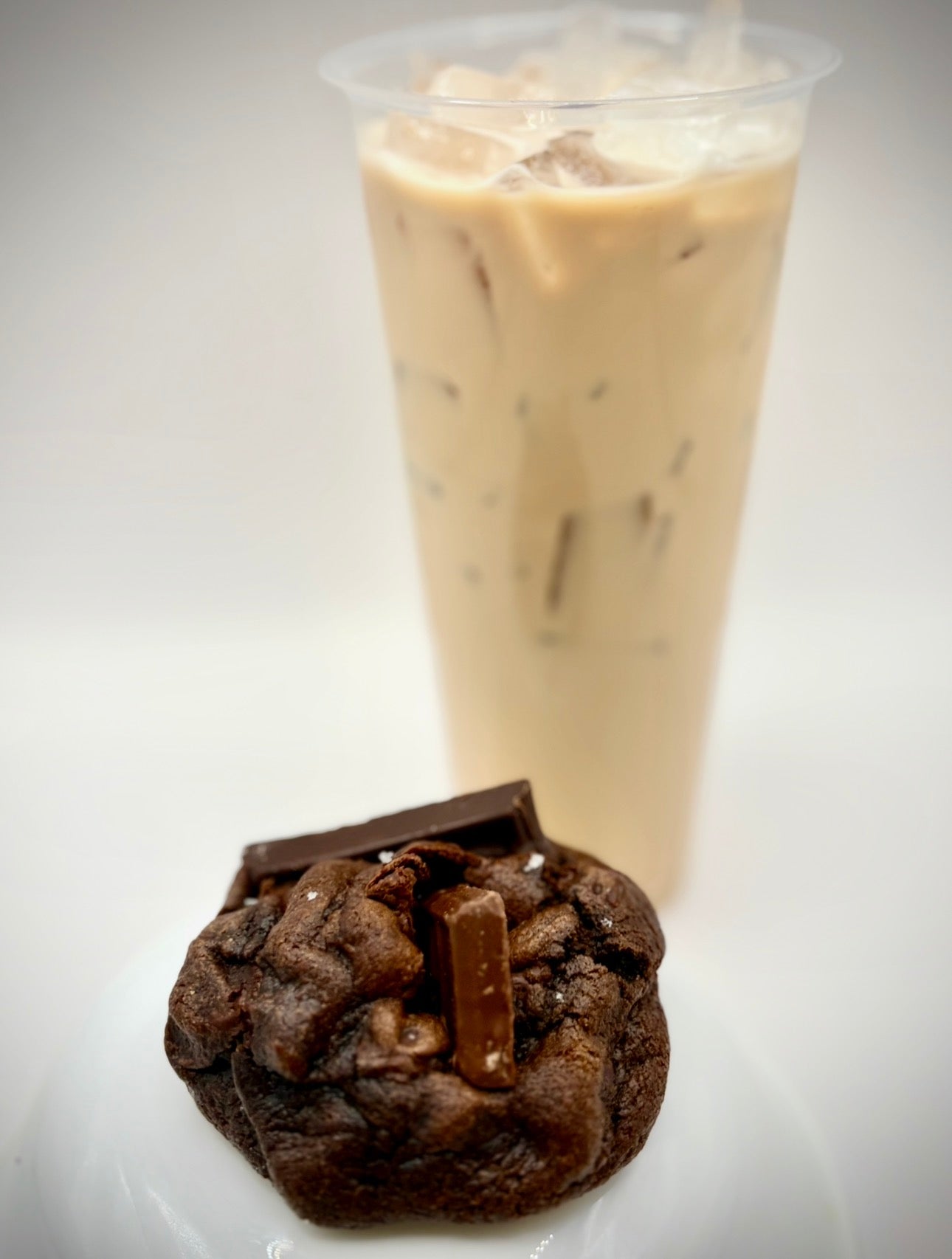 Chocolate cookie with a piece of chocolate on top next to an iced coffee drink.